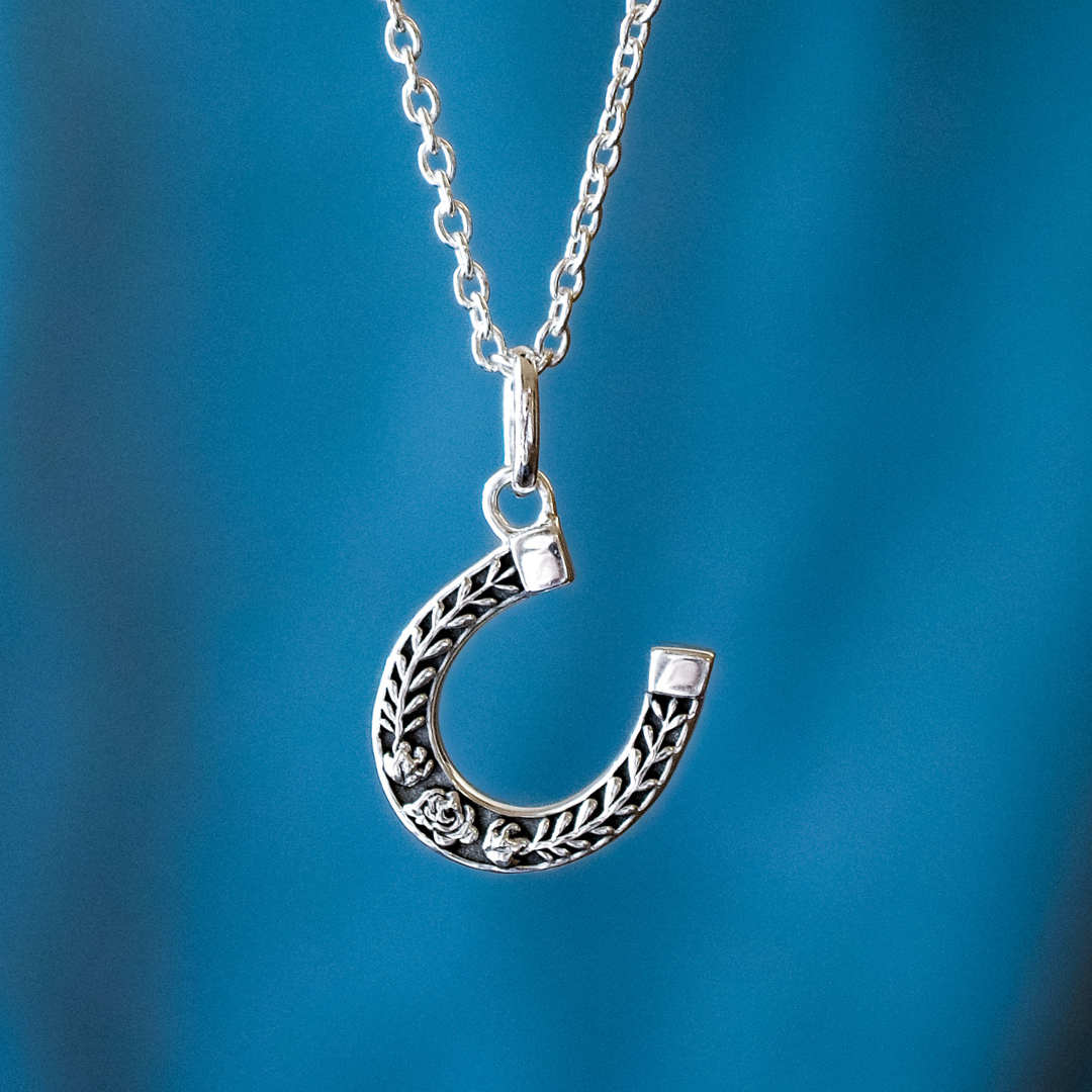Horseshoe Necklace with laurel and gardenia details hanging on a silver chain.