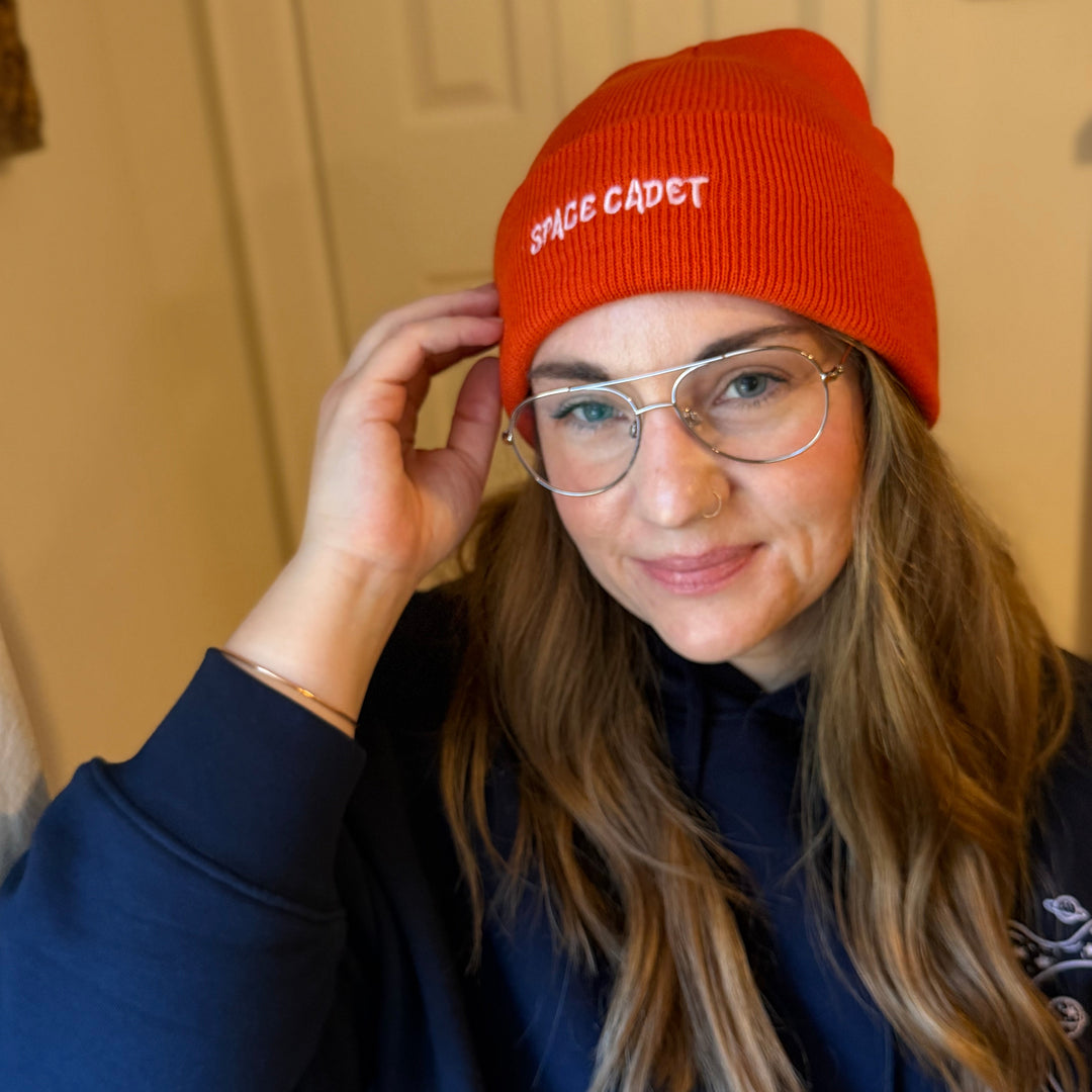 orange beanie with 'space cadet' embroidered in pink thread